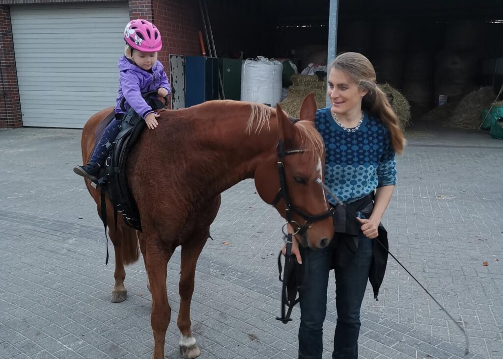 Kind auf braunen Pony. Frau führt Pony mit Kind darauf.